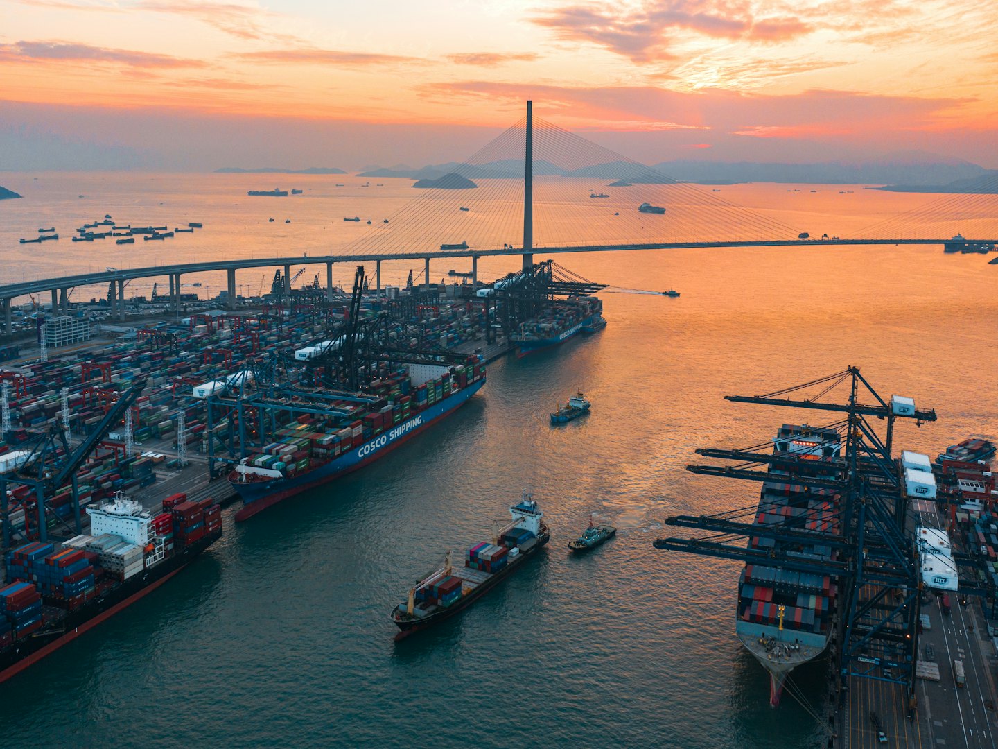 Porto container con navi e gru al tramonto vicino a un ponte.